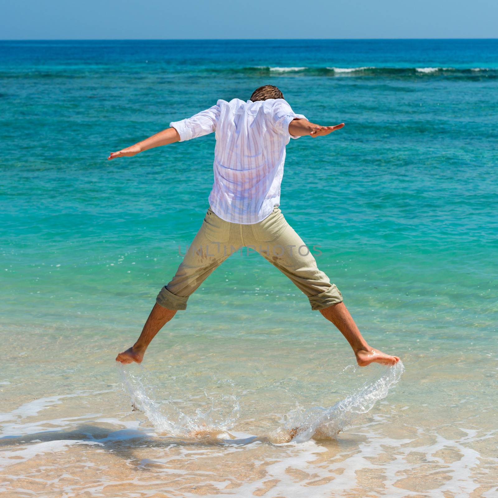 Man has fun in the blue sea by jumping up and spashing water