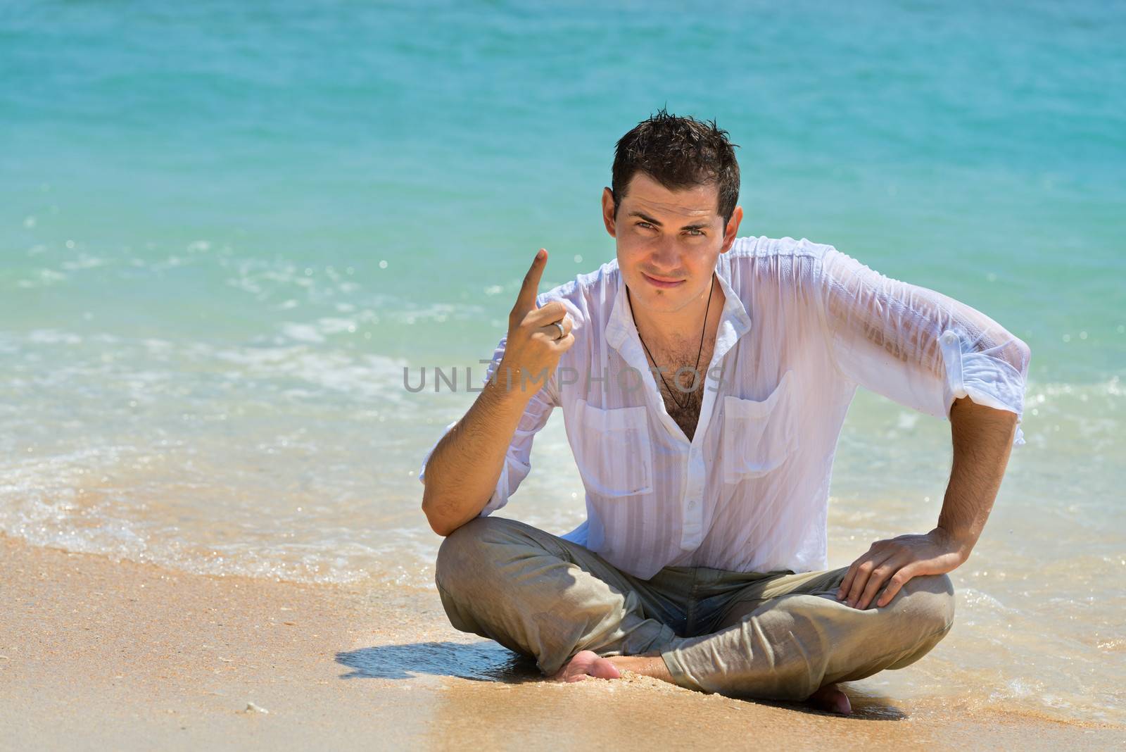 Serious young man sit on a beach near blue water with teaching and instructing gesture
