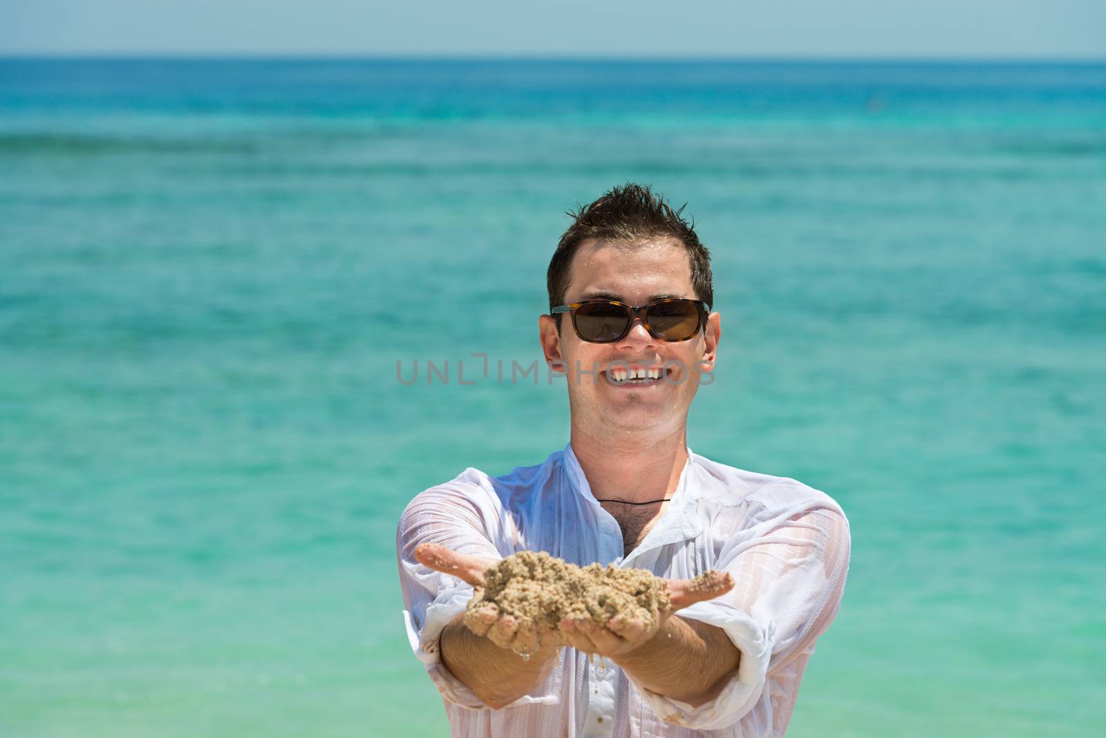 Smiling happy man in sunglasses hold a sand with blue sea on background