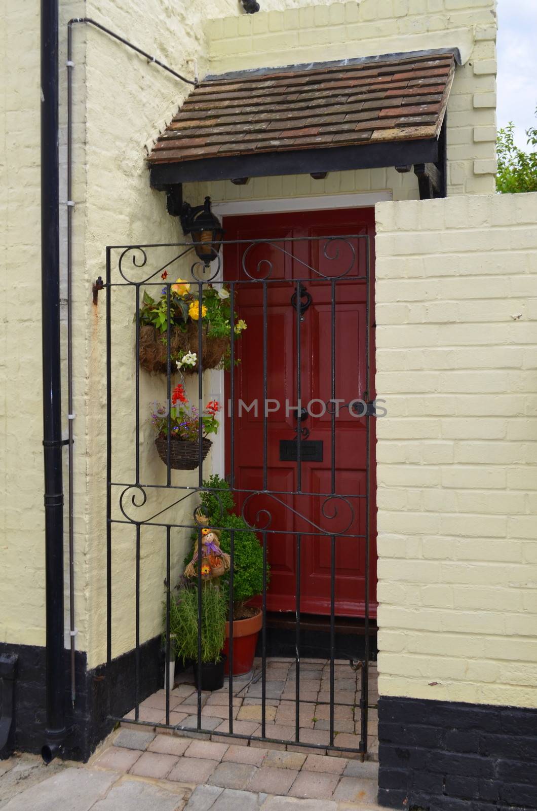 Red front door on a old cottage with flowers and a ornate iron gate in front of entrance.