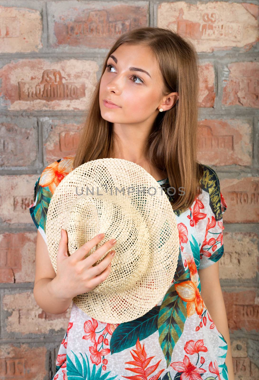 Portrait of pensive girl with a straw hat in hand against a vintage brick wall.