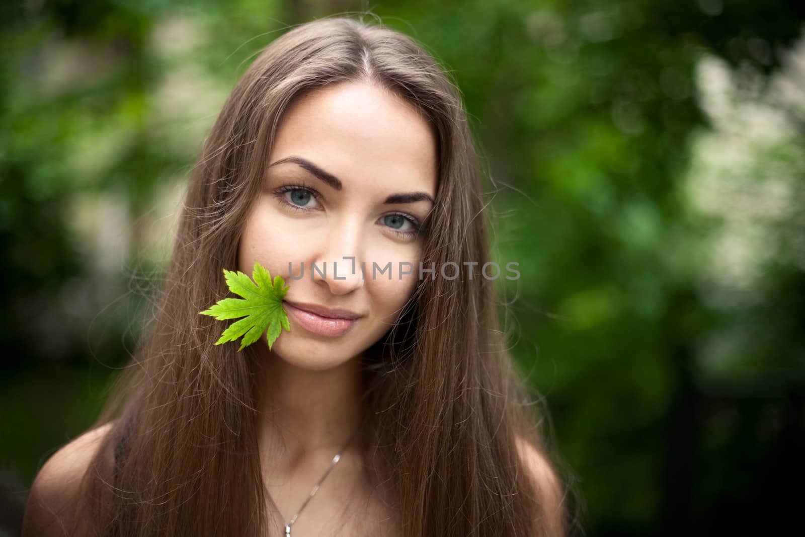 Beautiful girl with a maple leaf in her mouth. Green leaves  background. Nature.