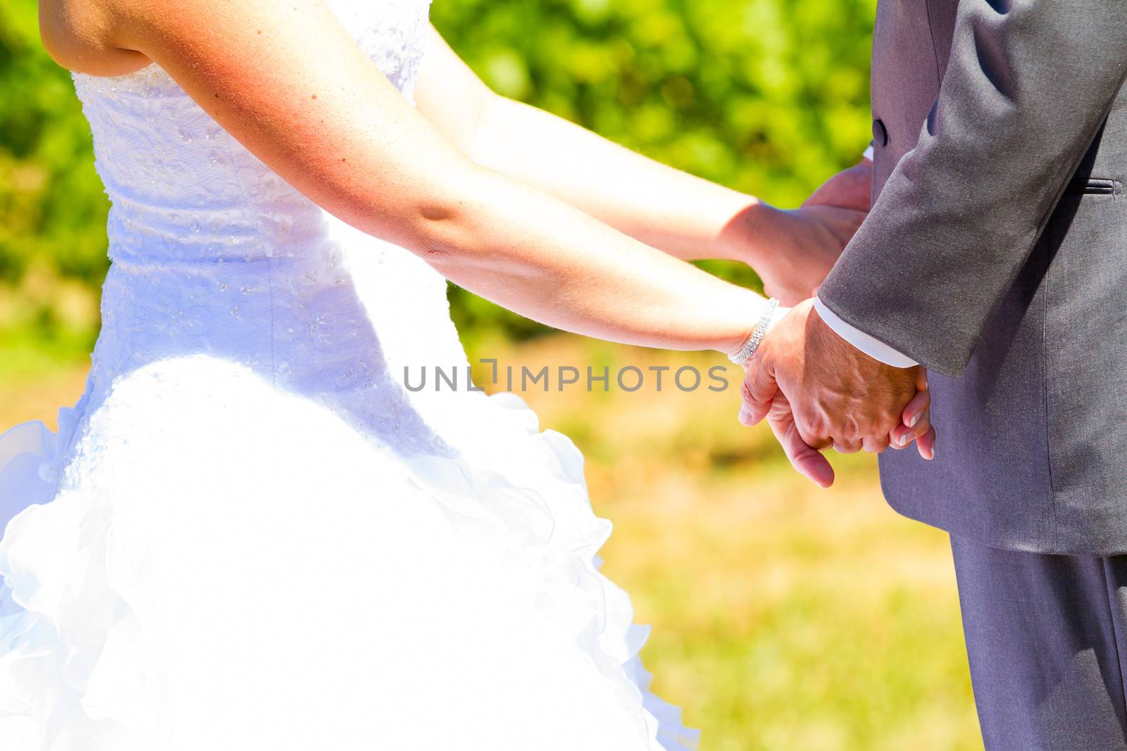 A bride and groom are close together showing just their torso arms and hands while holding each other after their wedding.