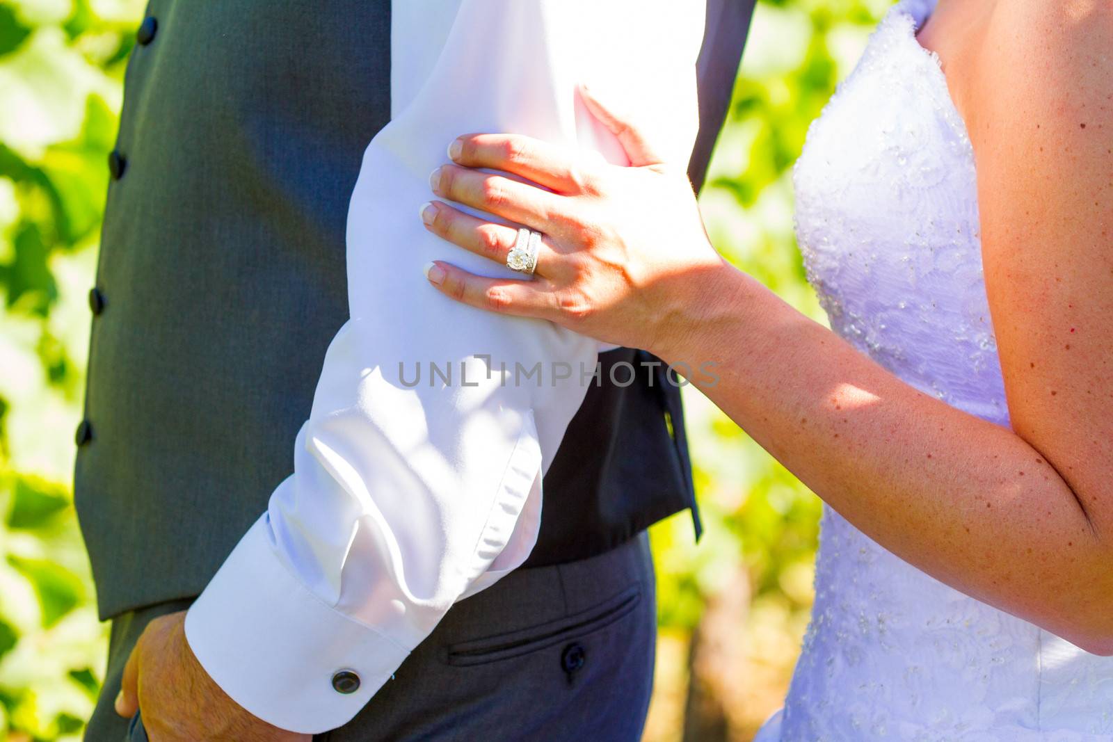 A bride and groom are close together showing just their torso arms and hands while holding each other after their wedding.