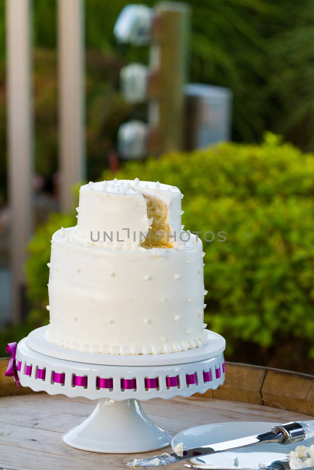 A white wedding cake is cut after the bride and groom cut the cake at their wedding reception.