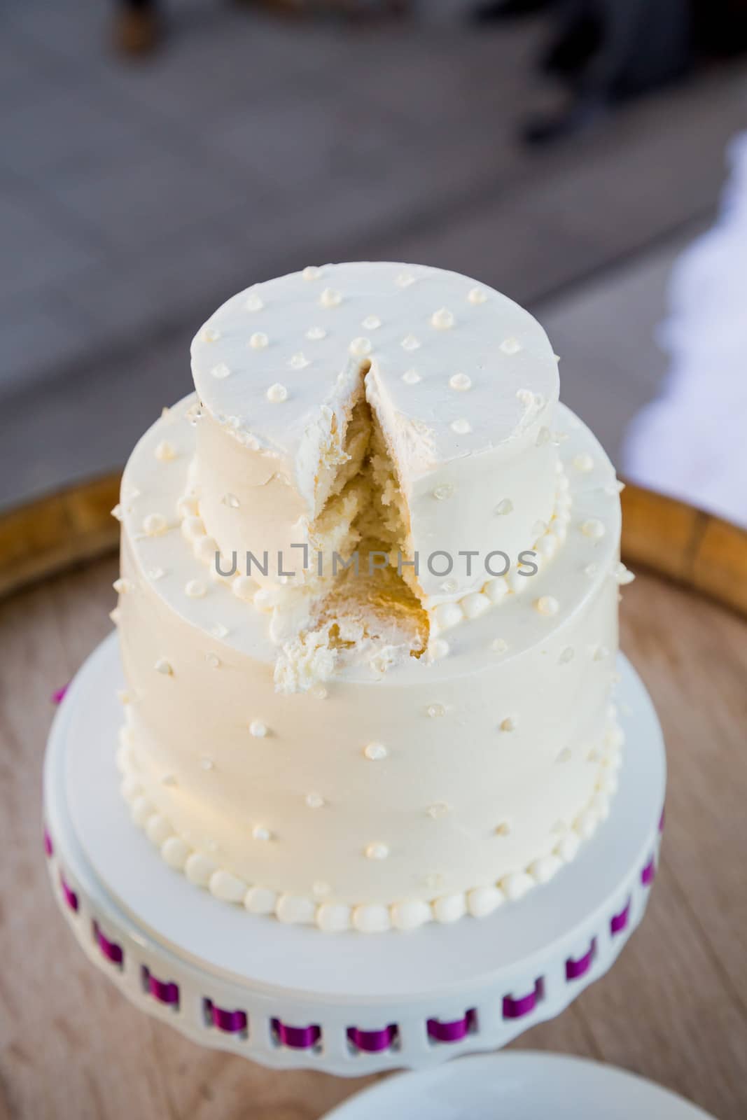 A white wedding cake is cut after the bride and groom cut the cake at their wedding reception.