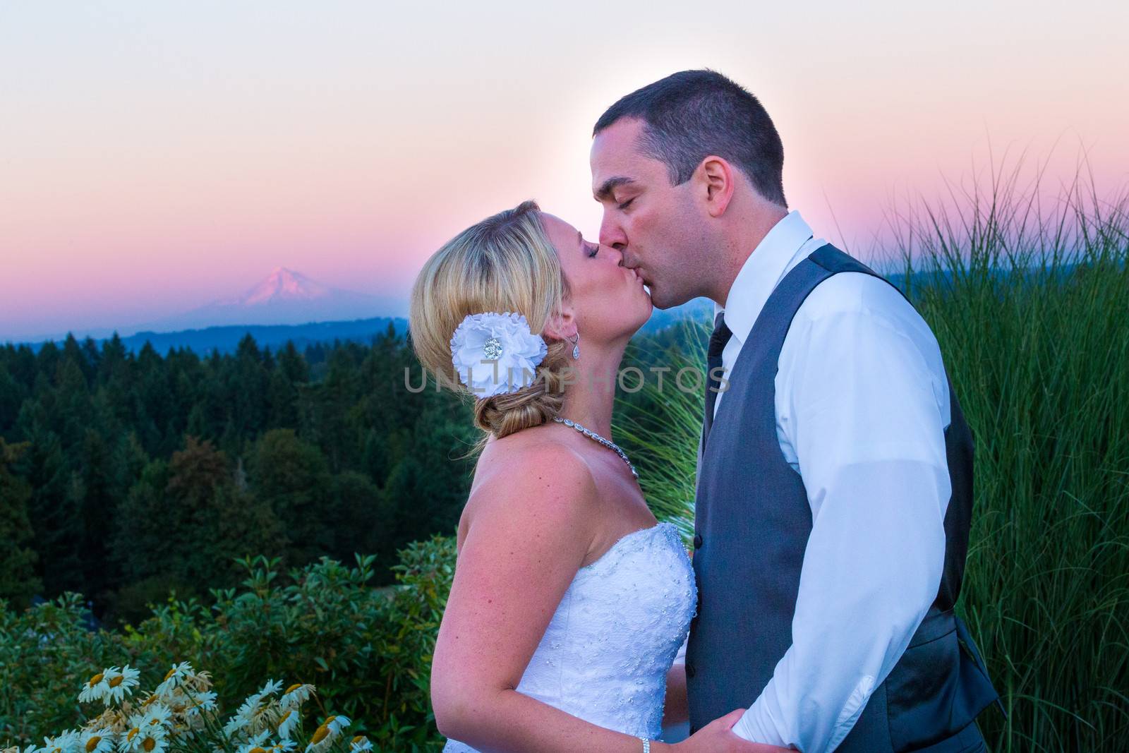 A bride and groom kiss during sunset with Mount Hood in the background at their wedding.