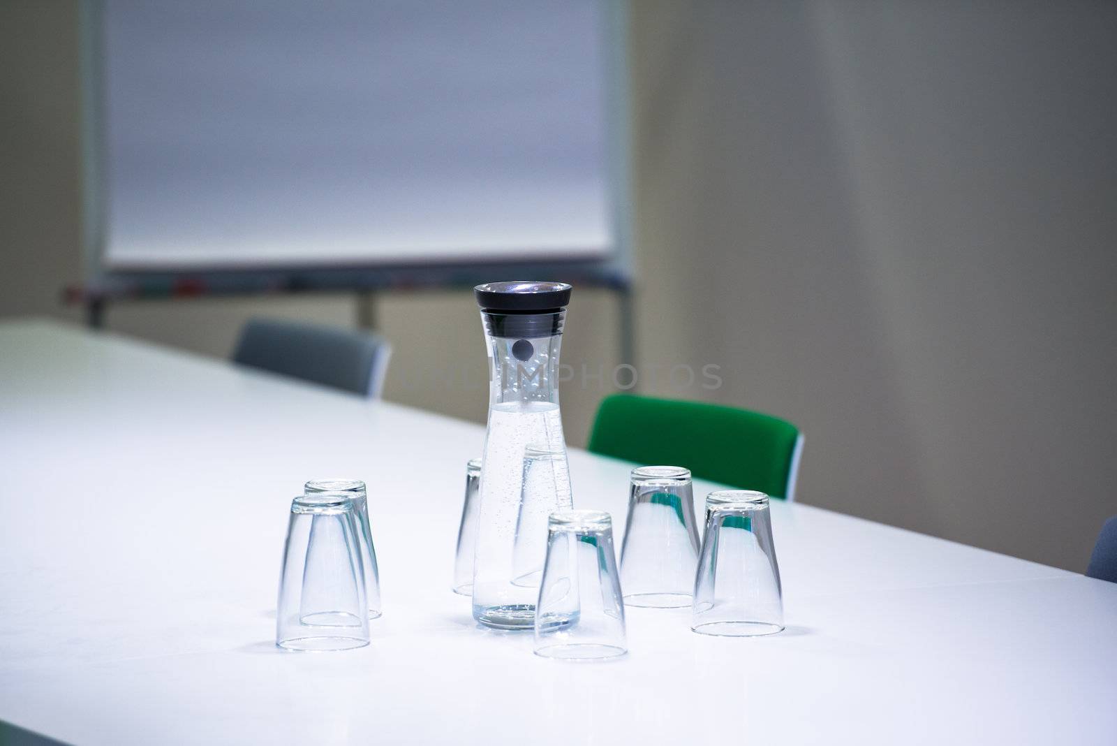 Ready for meeting: Water bottle and 6 glasses on a table with flipchart and chairs in conference room