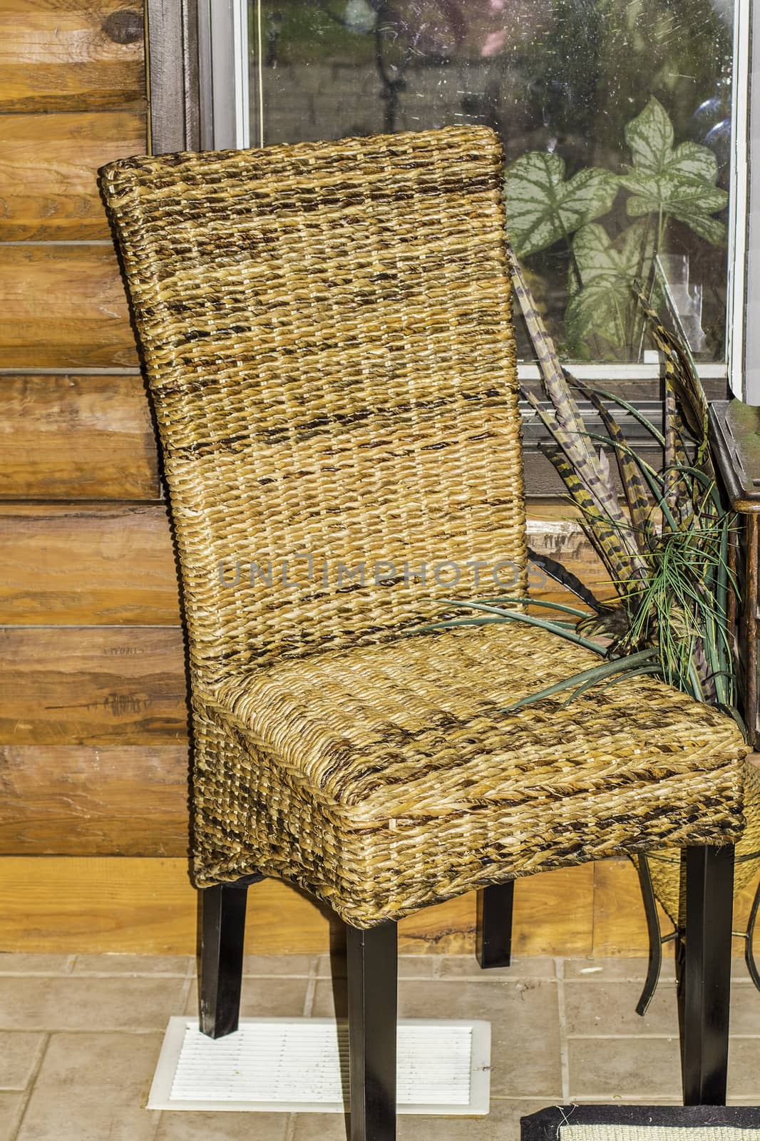 A wicker material chair sitting by a window in a log cabin.
