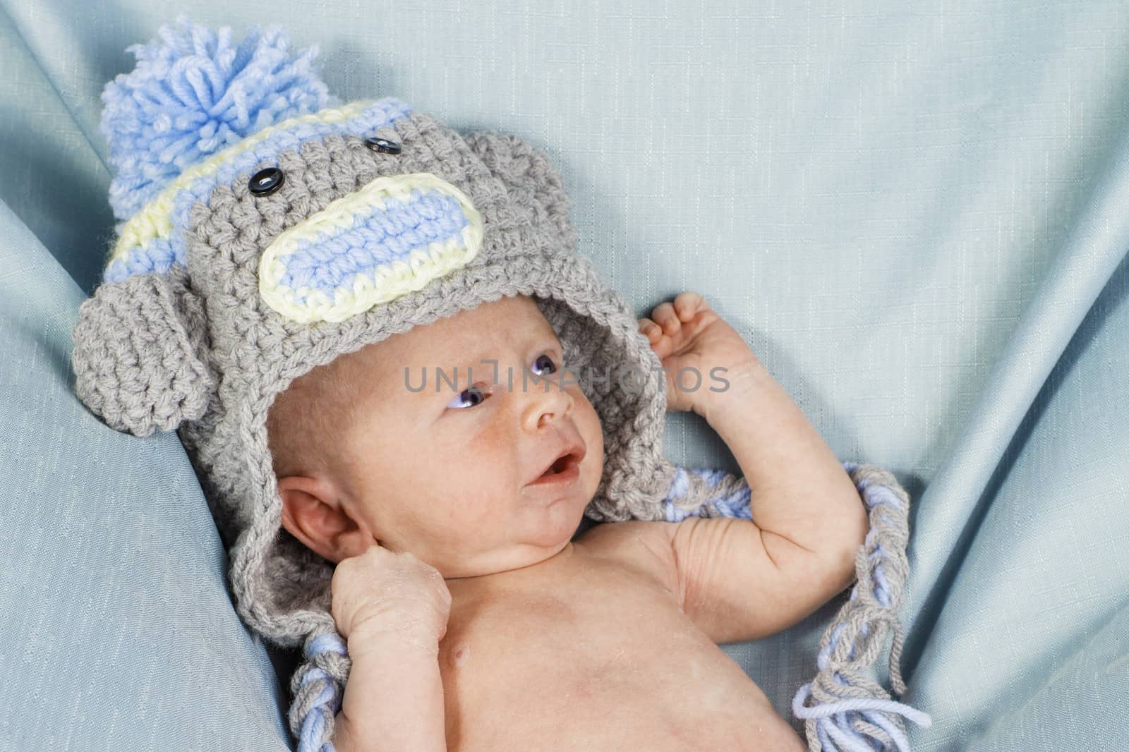 A newborn boy wearing a knitted hat laying on a blue blanket.