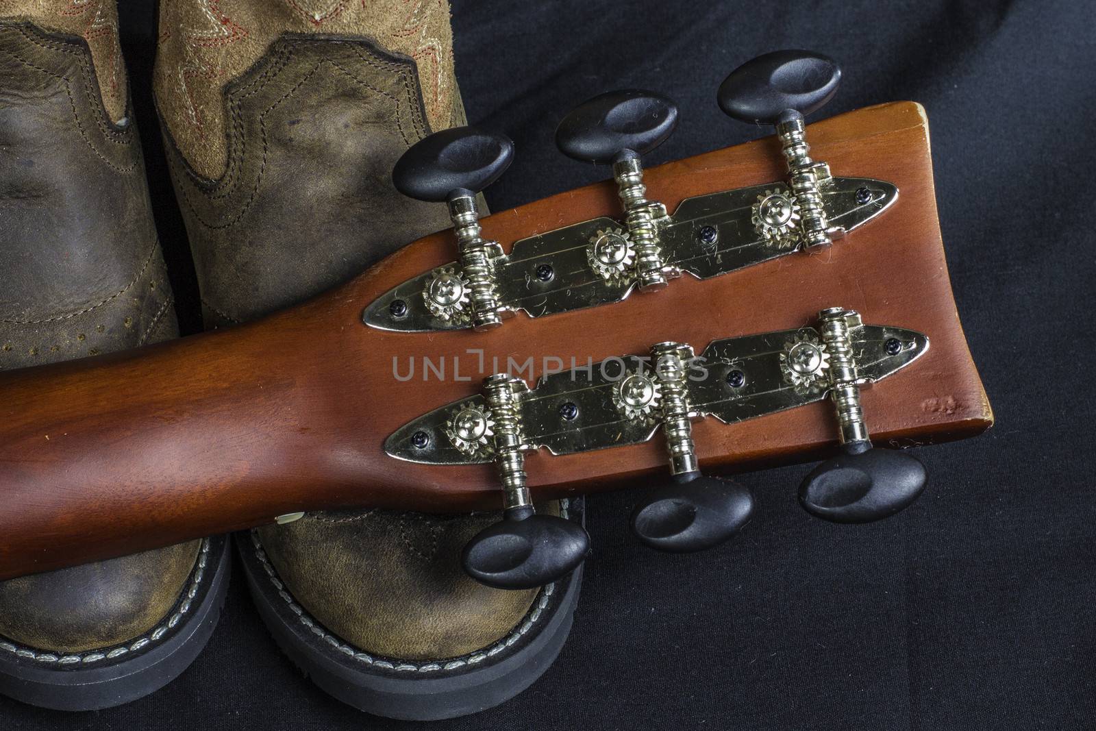 A close shot of a pair of boots and a cowboy guitar handle.
