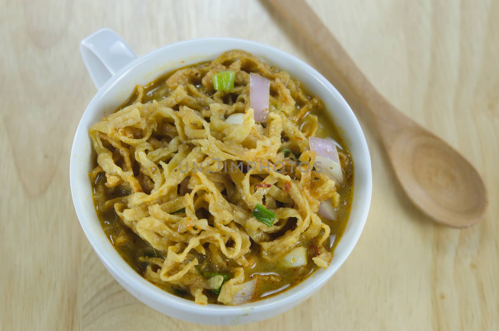 noodle dish in a yellow curry in white bowl on wooden background with spoon