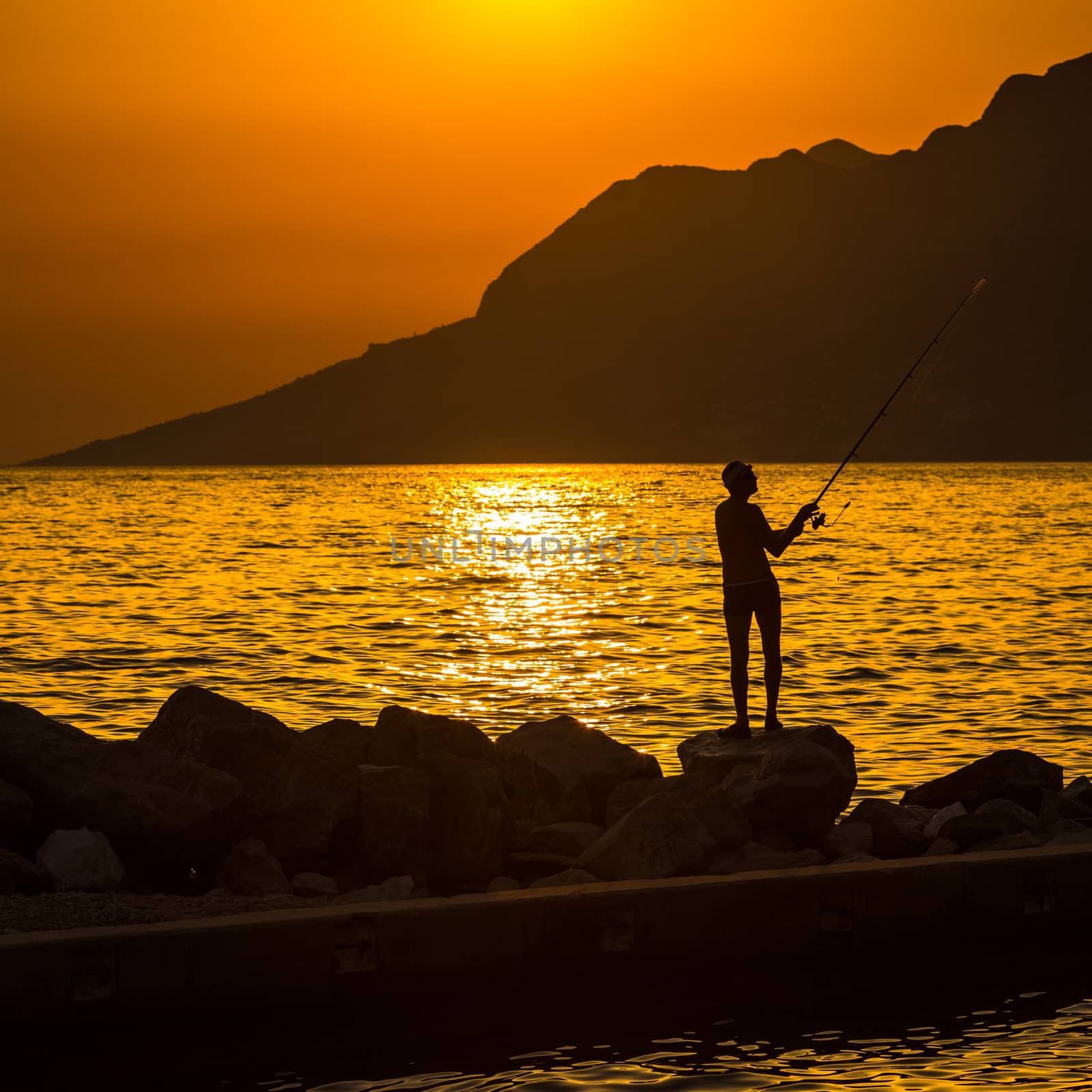 Fisherman silhouette on the beach at colorful sunset