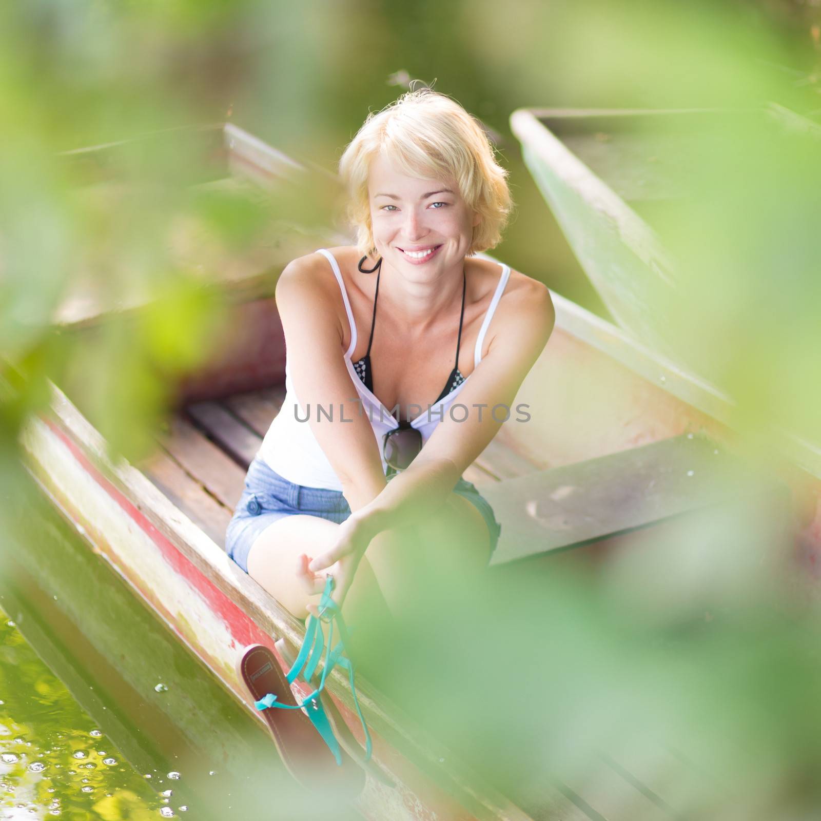 Carefree young blonde woman enjoying the sunny summer day on a vintage wooden boats on a lake in pure natural environment on the countryside.