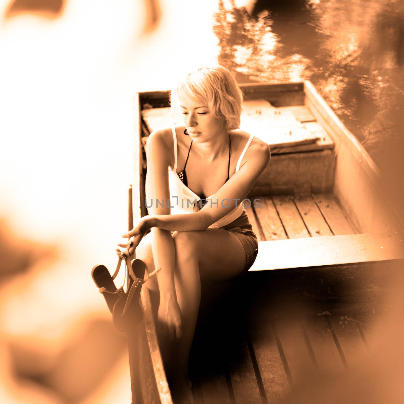Thoughtful young blonde woman enjoying the sunny summer day on a vintage wooden boats on a lake in pure natural environment on the countryside. Vintage sepia toning.