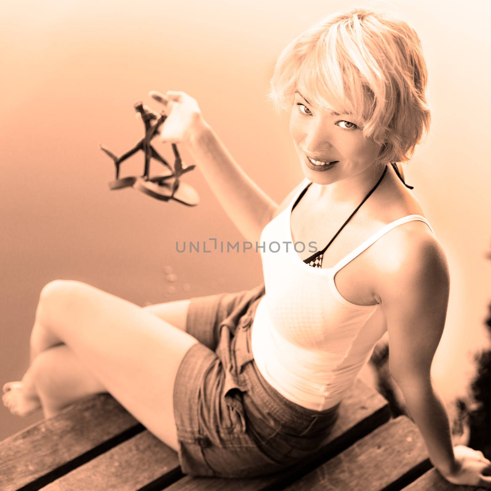 Romantiimage of beautiful carefree young blonde woman enjoying the sunny summer day on a vintage wooden pier on a lake in pure natural environment on the countryside; retro sepia toning.