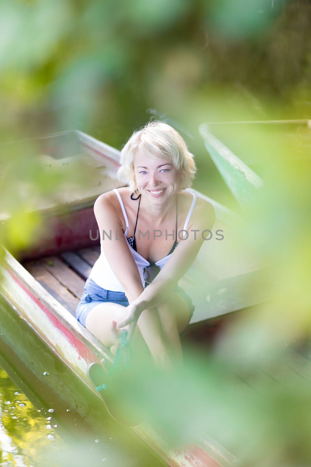 Relaxed young blonde woman  enjoying the sunny summer day on a vintage wooden boats on a lake in pure natural environment on the countryside.