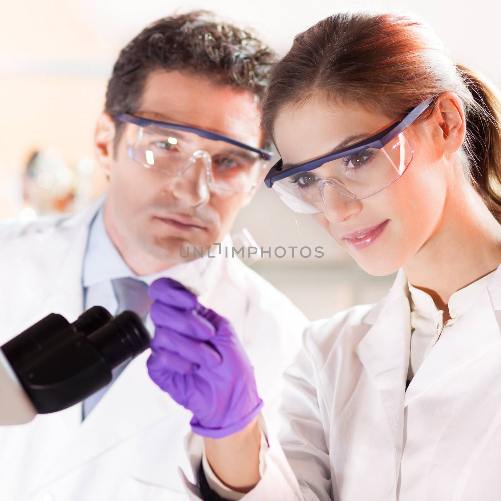 Attractive young scientist and her suprvisor looking at the microscope slide in the forensic laboratory.