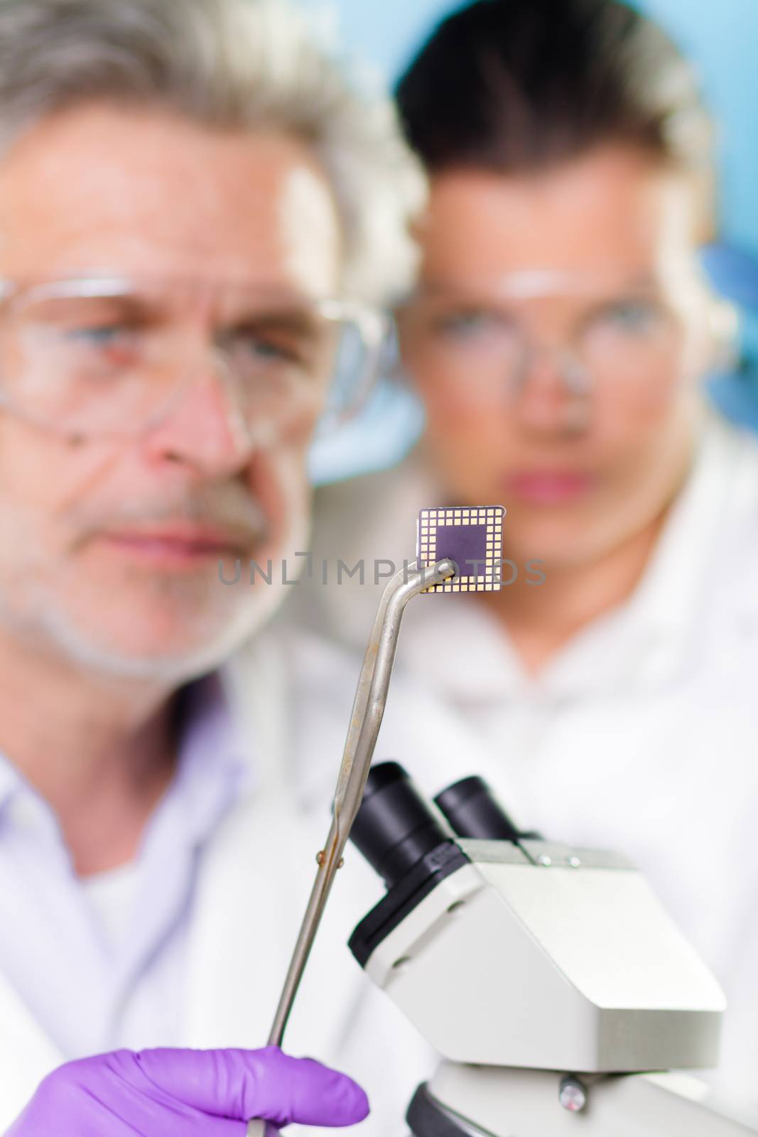 Focused senior  engineer holding and showing the micro chip to his student.  Lens focus on the chip.