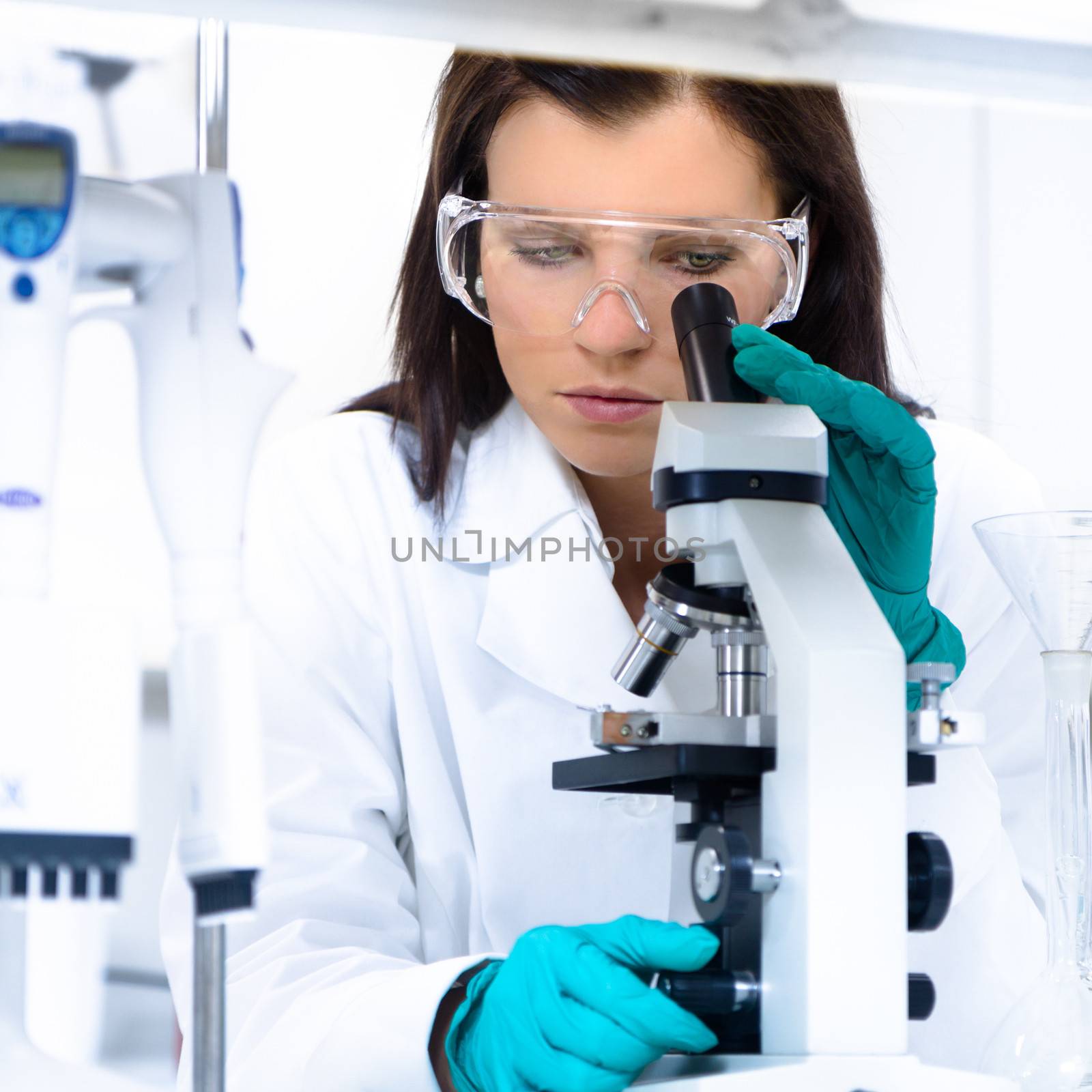 Attractive young PhD student scientist looking at the microscope slide in the life science research laboratory (biochemistry, genetics, forensics, microbiology ..)