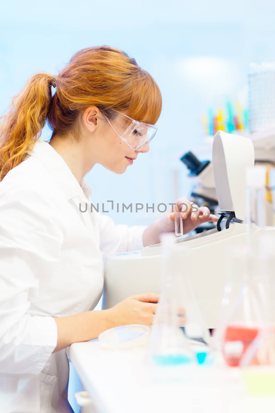 Focused attractive young life science professional measuring the absorbance of the solution in cuvette in the spectrophotometer. Focus on the researcher's face.