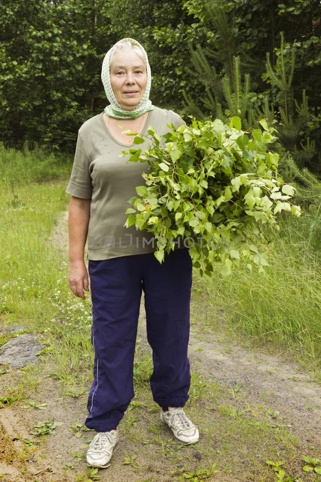 Mature beautiful woman with birch brooms on the forest glade