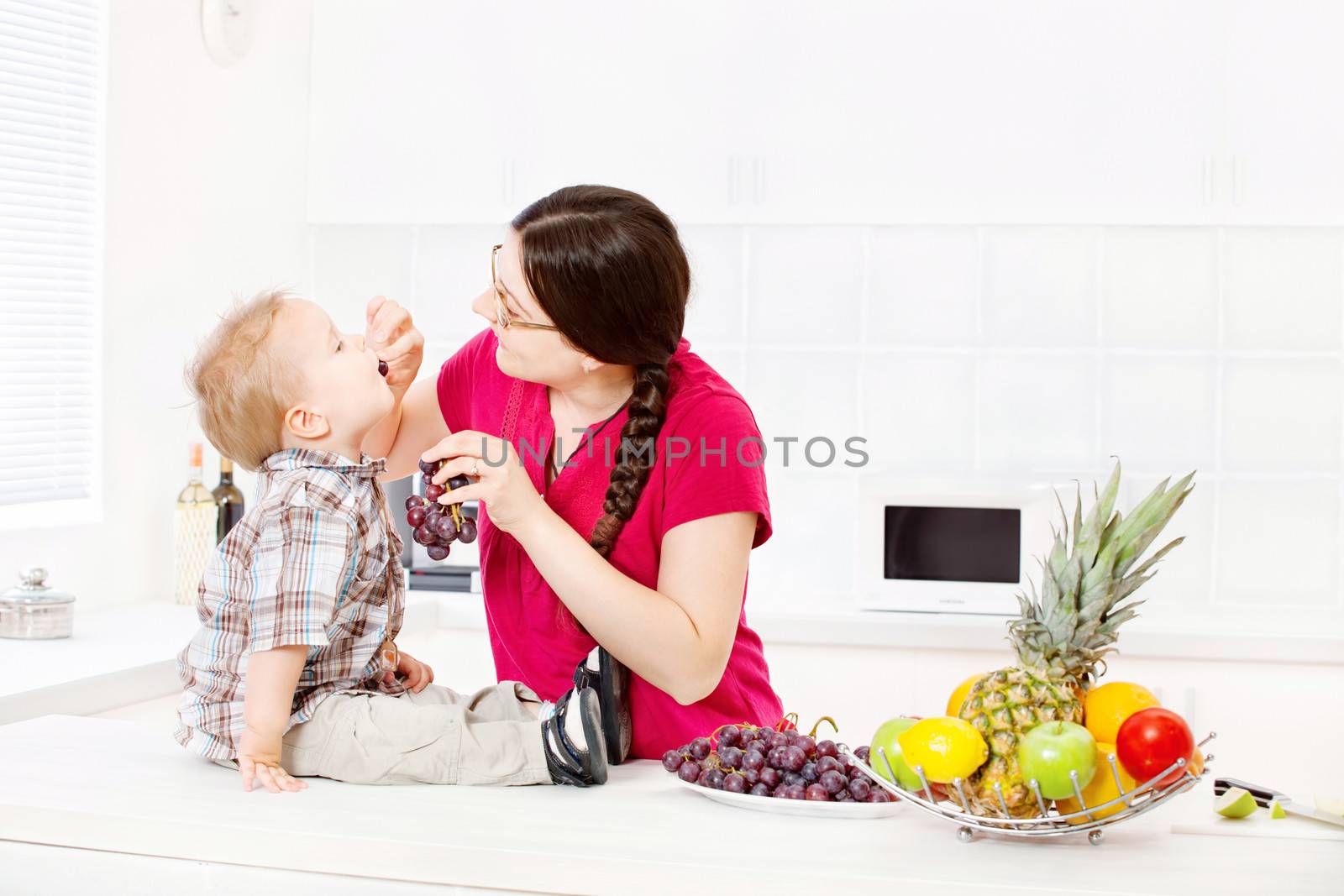 Mother feeding child with grapes in kitchen