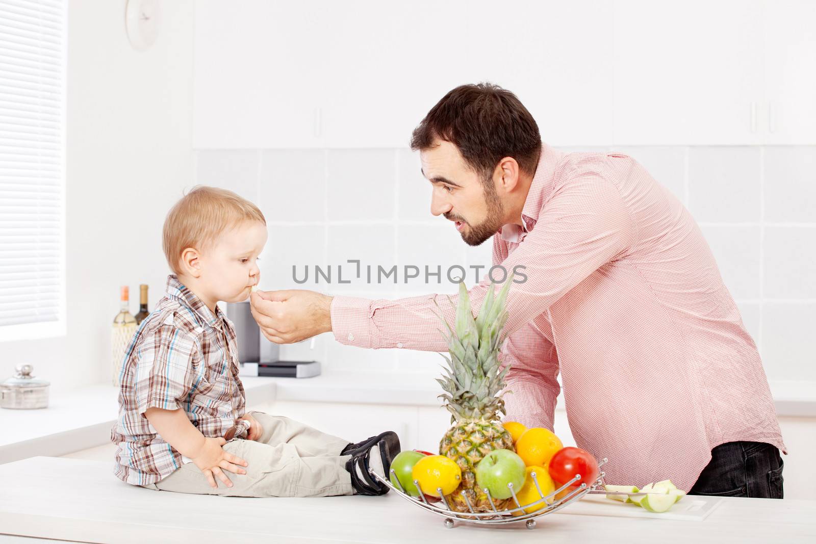Father feeding child with apple in kitchen