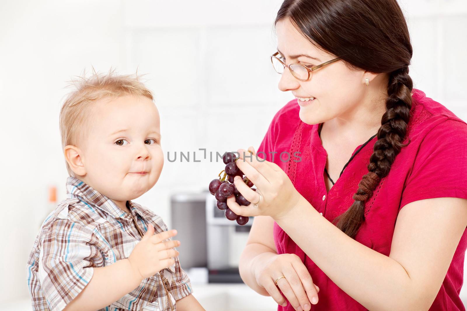 Mother feeding child with grapes in kitchen