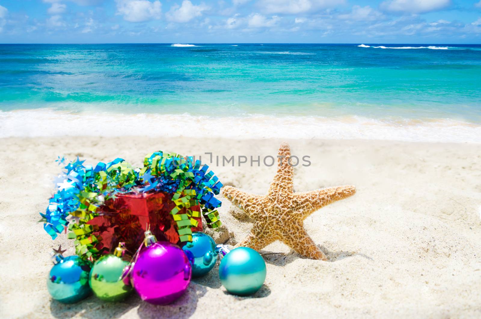 Starfish with Christmas balls and red gift box on sandy beach in sunny day- holiday concept