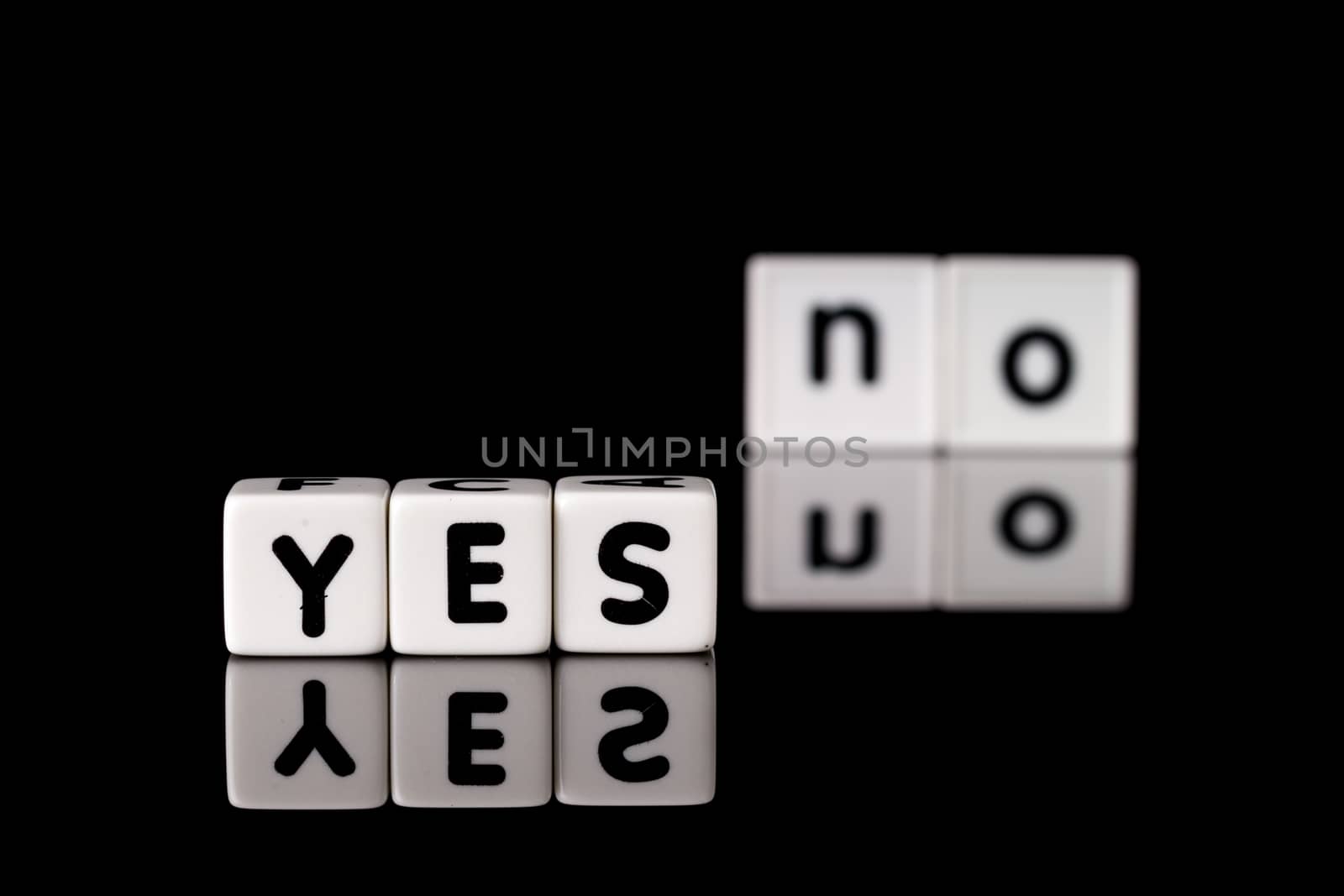 Yes spelled in dice letters in foreground with the word no out of focus in background. Isolated on black background.