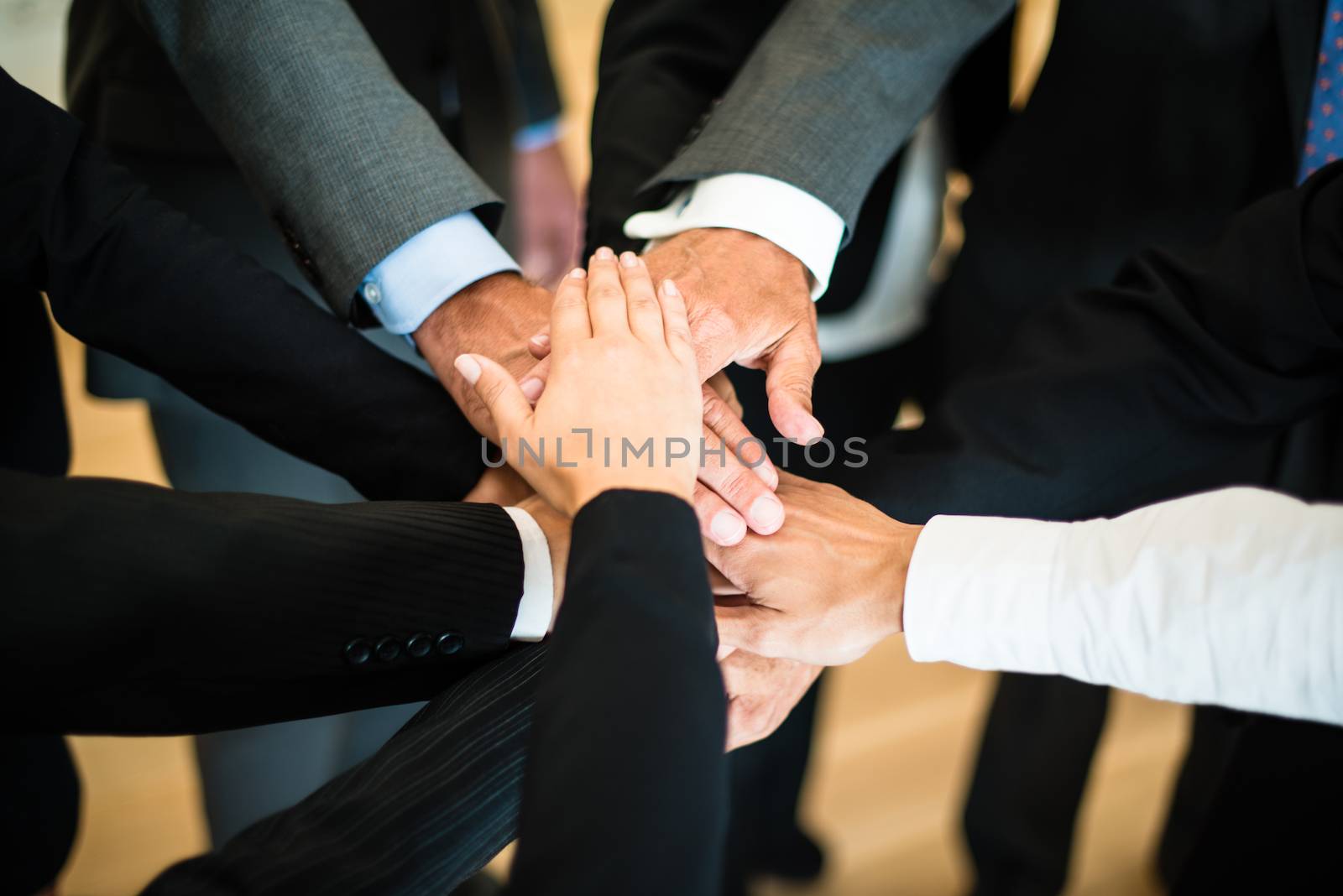 Multiracial group of nine diverse businesspeople standing in a circle facing each other joining hands in a team