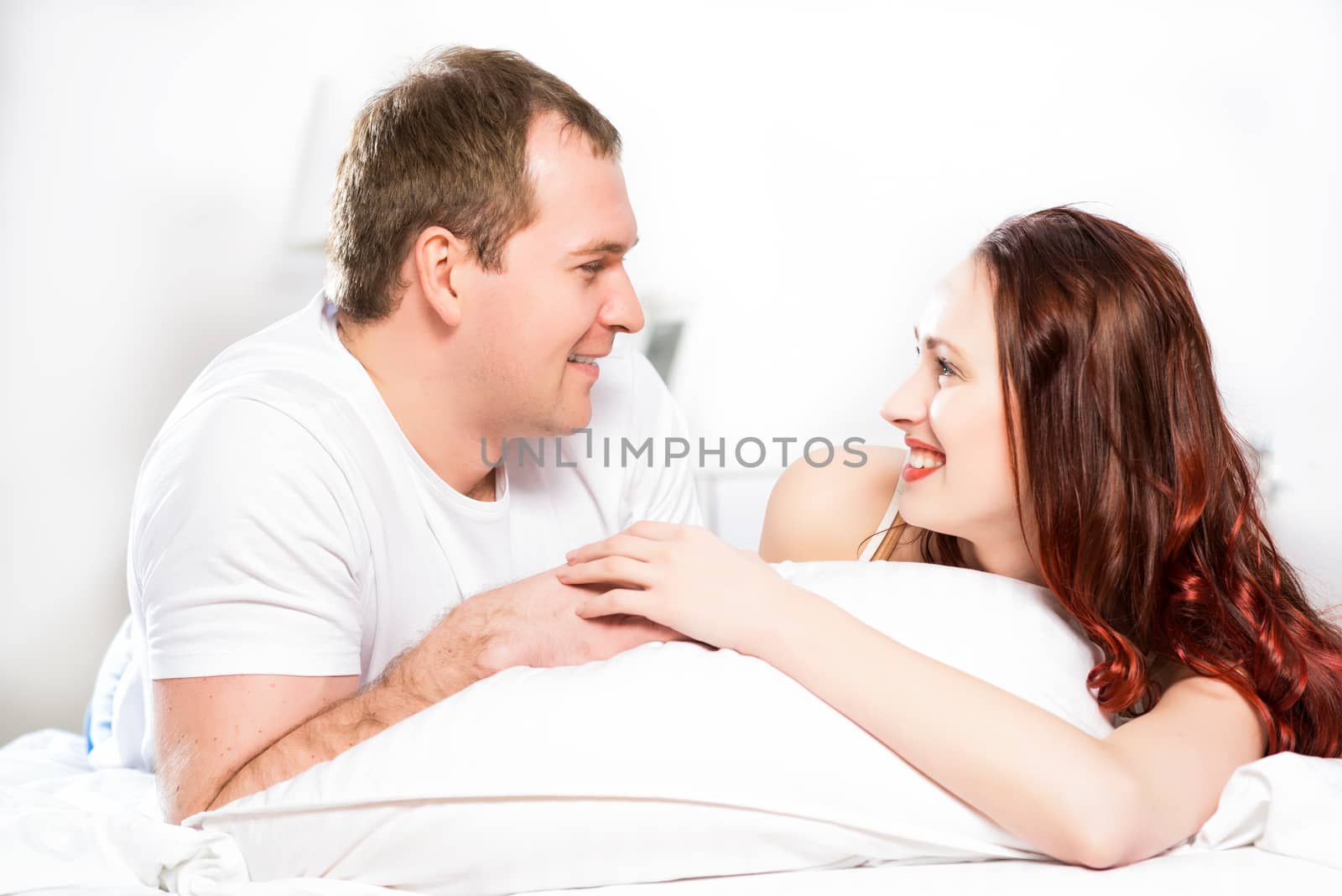 Young man and woman lying together in bed, smiling and happy