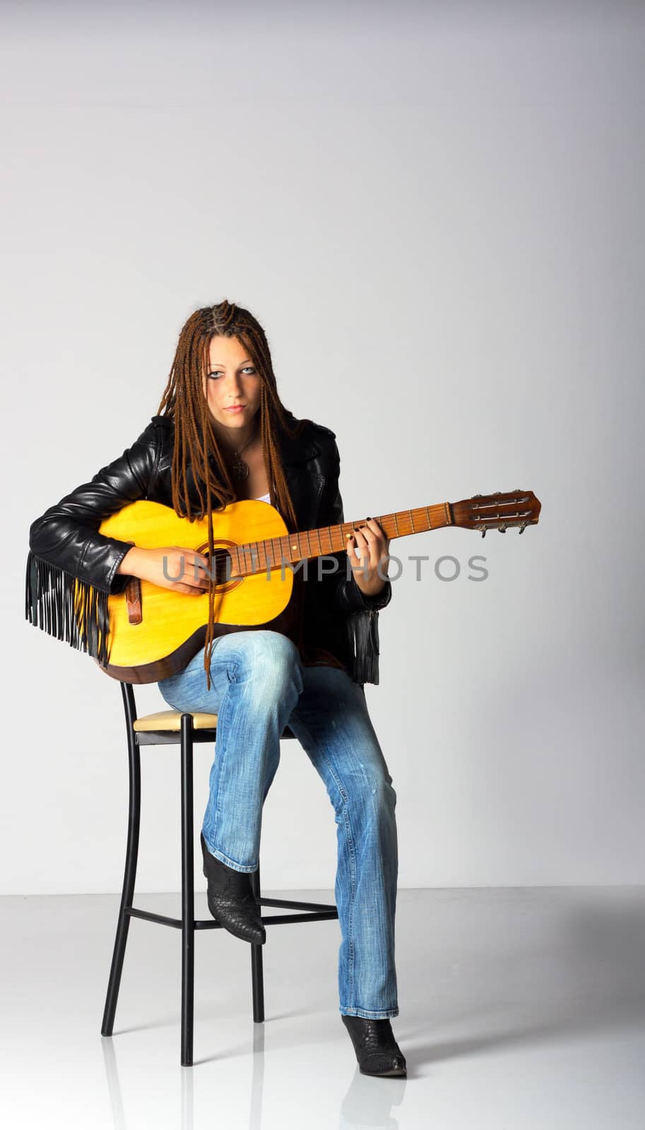 girl in black jacket and blue jeans with guitar sitting on the chair