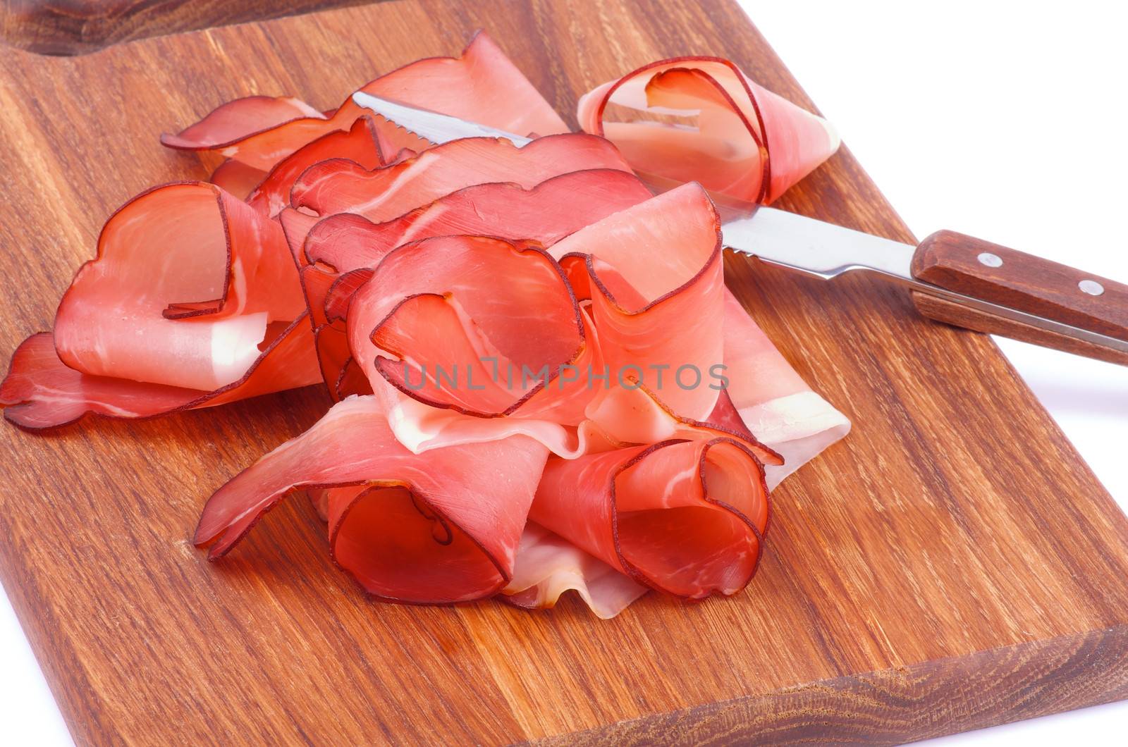 Heap of Prosciutto Slices and Kitchen Knife on Wooden Cutting Board closeup on white background