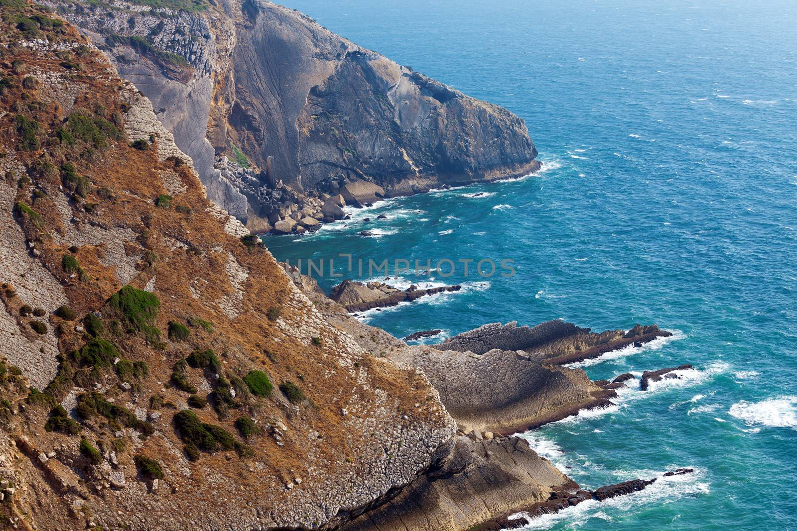 View of a rugged coastline with steep barren cliffs falling down to a rocky shoreline with waves