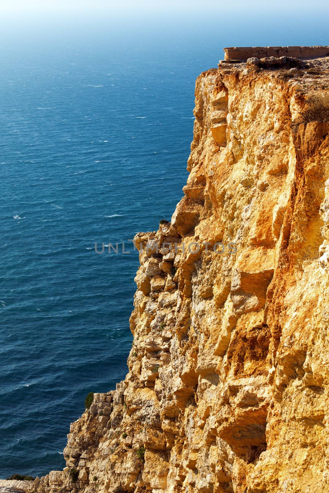 View of a rugged coastline with steep barren cliffs falling down to a rocky shoreline with waves
