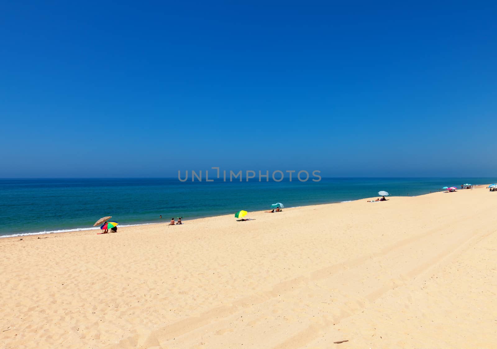 Beautiful tropical beach with bathers relaxing on an expanse of golden sand alongside a calm blue ocean in the summer sun