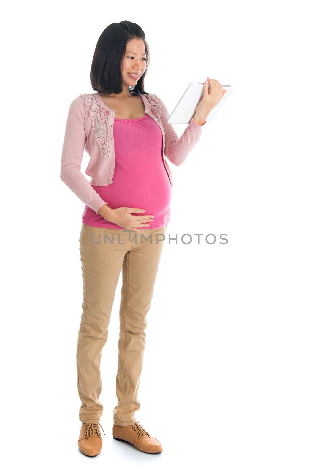 Full body six months pregnant Asian woman using digital computer tablet pc standing isolated on white background.