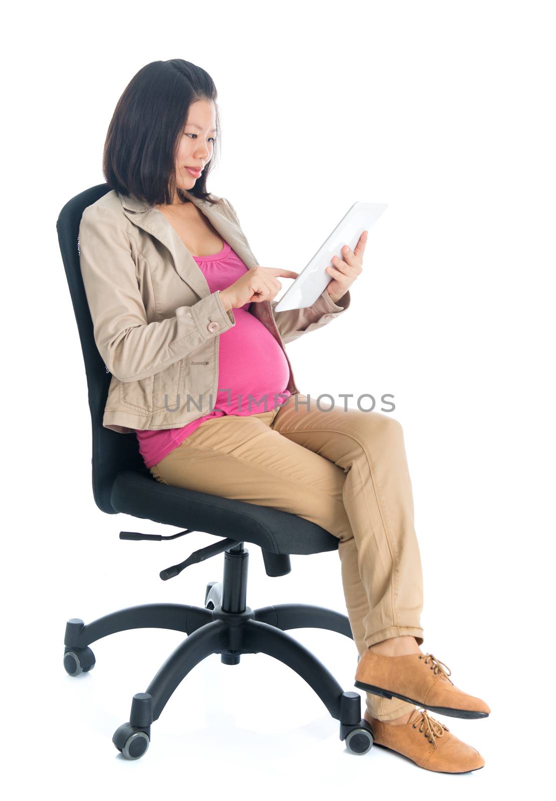 Full body six months pregnant Asian business woman using digital computer tablet pc, sitting on chair isolated on white background.