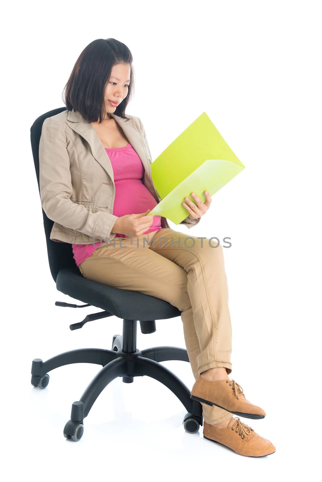 Full body six months pregnant Asian businesswoman reading file document sitting on chair, isolated on white background.