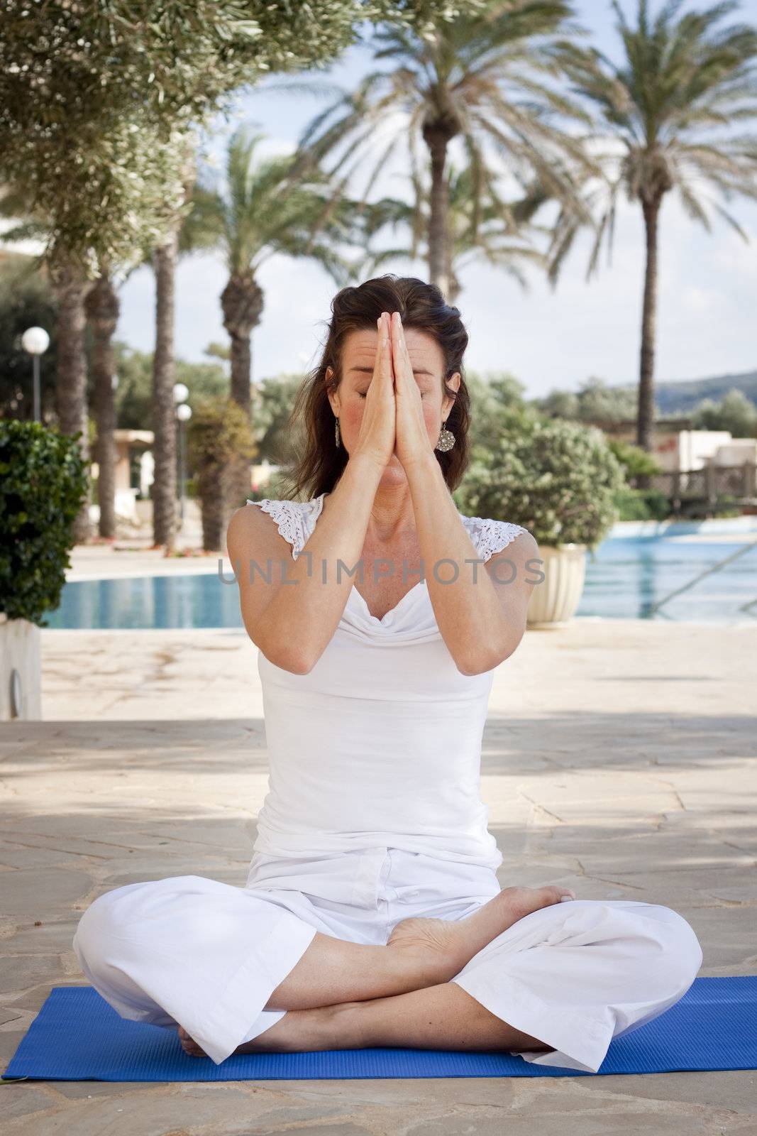 Woman meditating in lotus position with eyes closing, holding up hands in namaste greeting