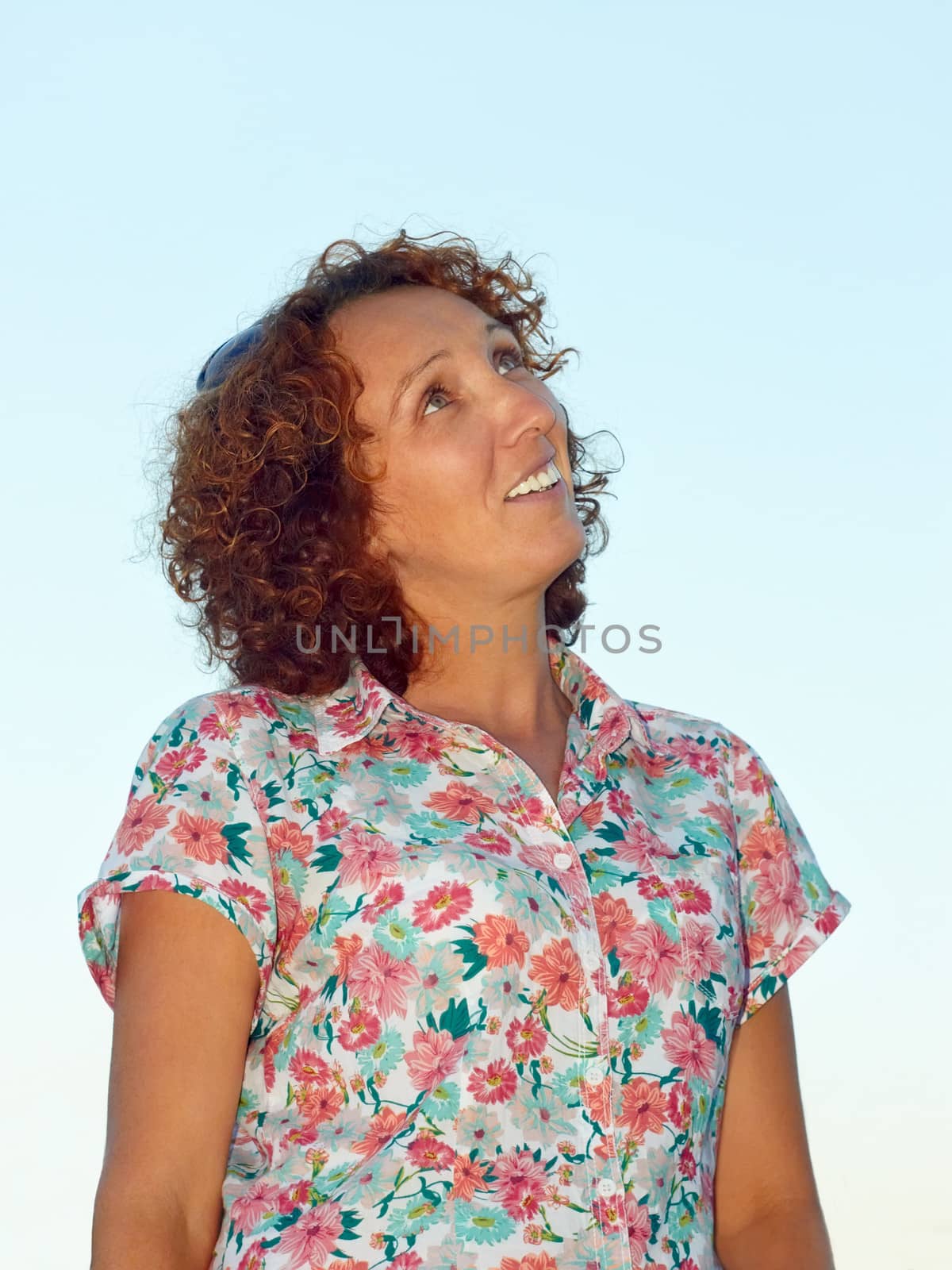 Joyful woman smiling and looking up against a light blue evening sky