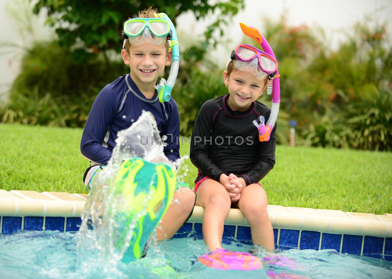 two children splashing water with swimming fins in pool