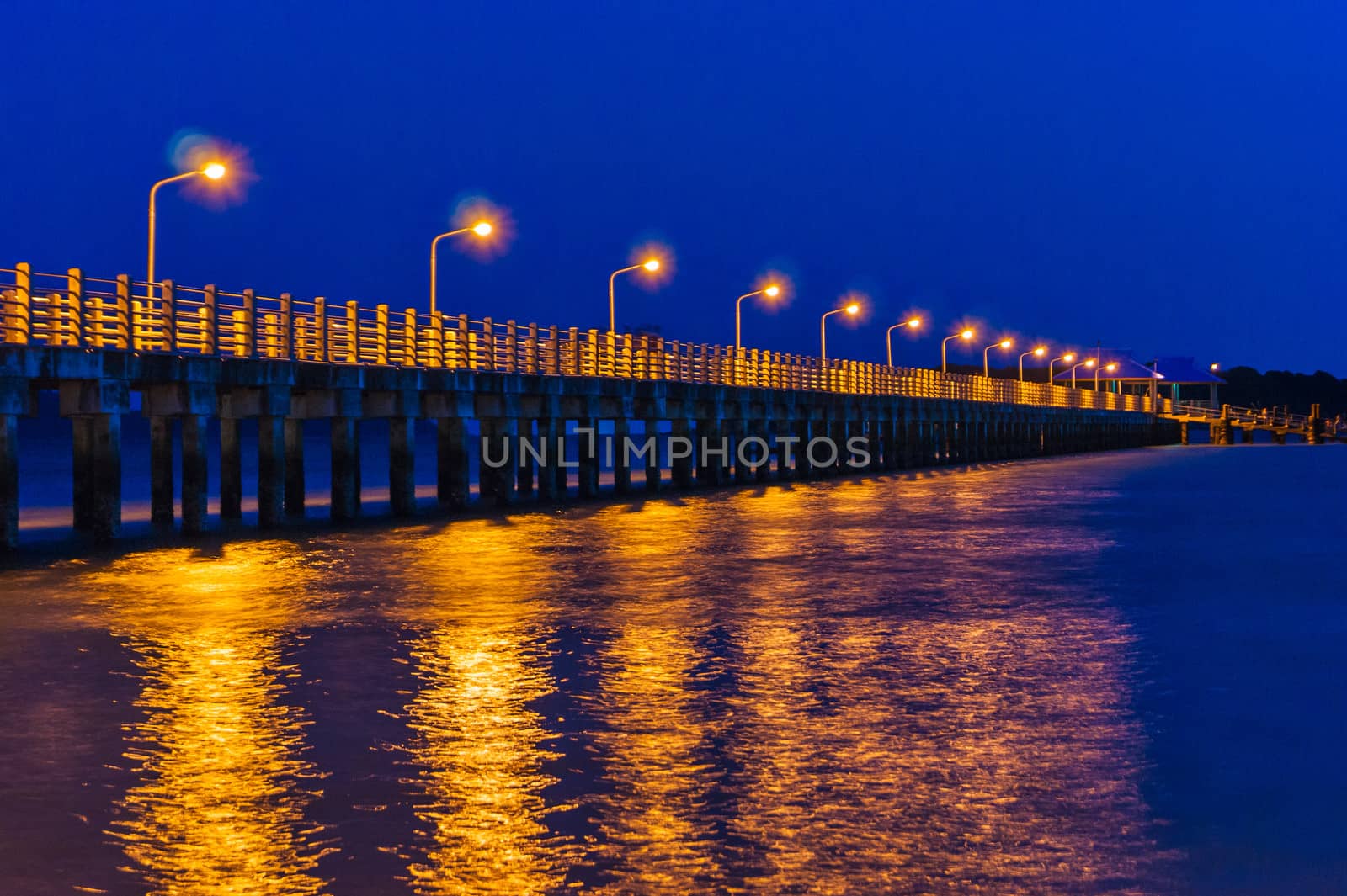 Pier at night with yellow lights on a background of blue sky stretching into the sea