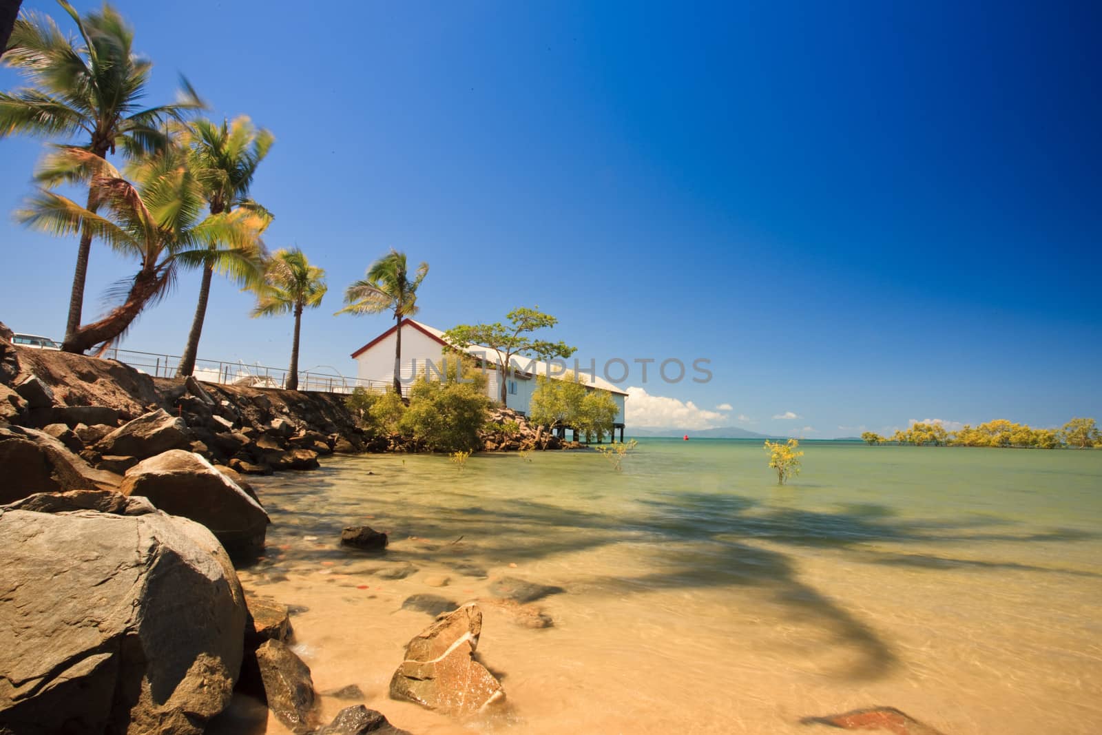 Beautiful tropical bay with palm trees and golden sand with a marine building built out over the water on a pier