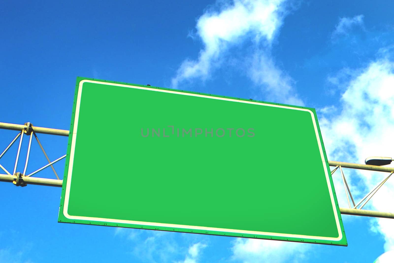 Blank green overhead traffic sign with copyspace for your text or destination against a cloudy sunny blue sky