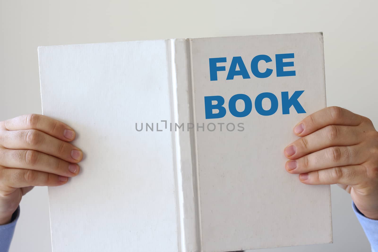 Man reading a book entitled Face Book holding it up in his hands so that his face is hidden behind the cover