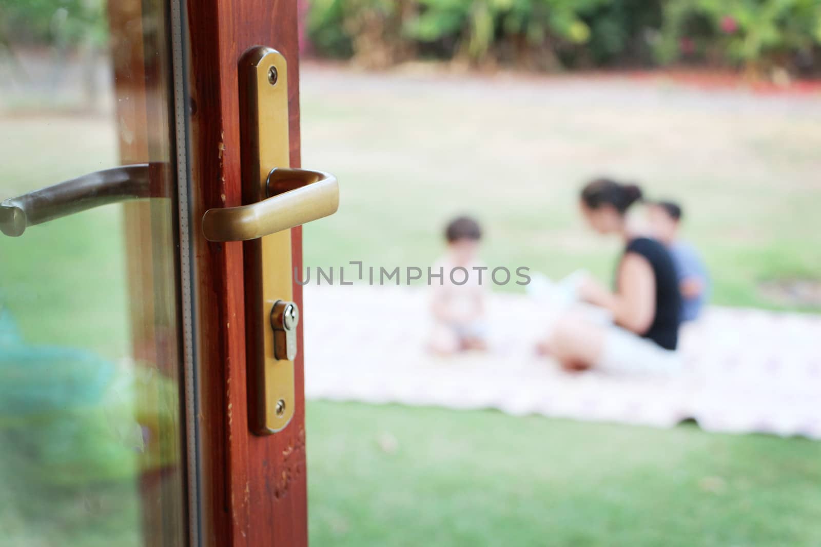 Young family sitting on the lawn viewed through an open door with focus to the handle conceptual of danger, safety and security