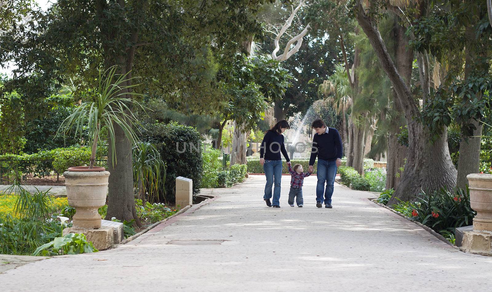 A baby boy of mixed race is walking with his parents in a colonial park